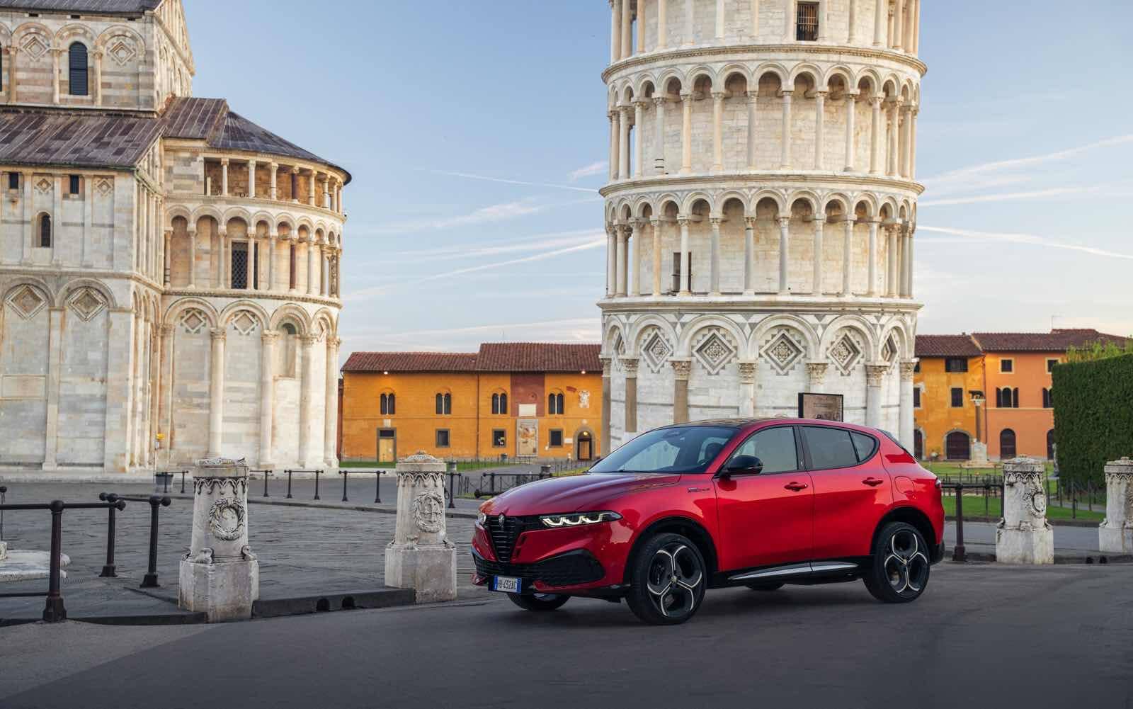 Alfa Romeo Tonale MY 2026 rossa davanti alla Torre Pendente di Pisa, monumento famoso in Italia, scenario iconico, design moderno, mercato automotive, modello innovativo, veicolo urbano, Italia.