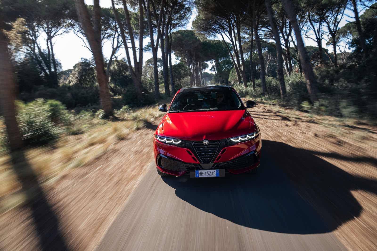 Alfa Romeo Tonale in movimento su strada forestale, SUV compatto di design sportivo e tecnologia avanzata.