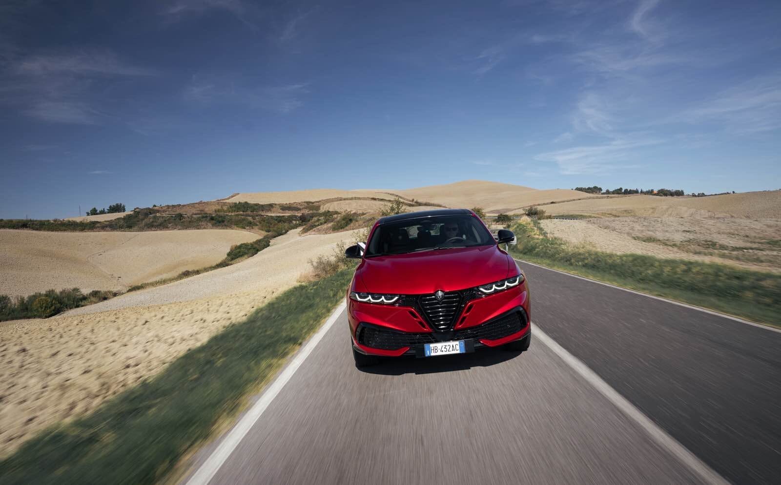 Auto Alfa Romeo Tonale MY 2026 rossa su strada panoramica in campagna, design moderno e performance.