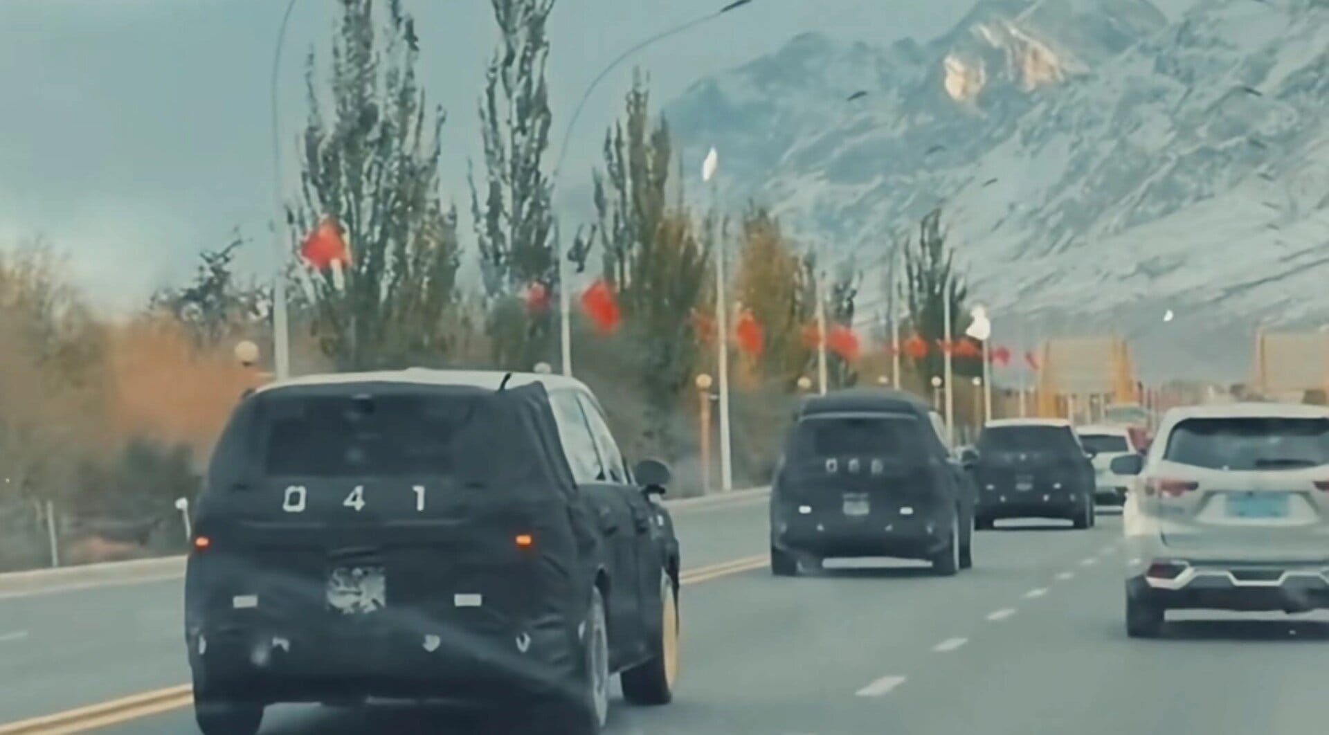 Automobile Xiaomi camuffata durante un test di prototipo su strada con montagne sullo sfondo.