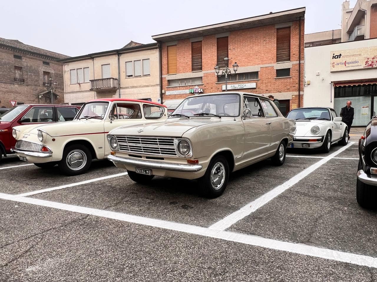 Vecchie auto d'epoca parcheggiate in una piazza in Italia con edifici storici sullo sfondo.