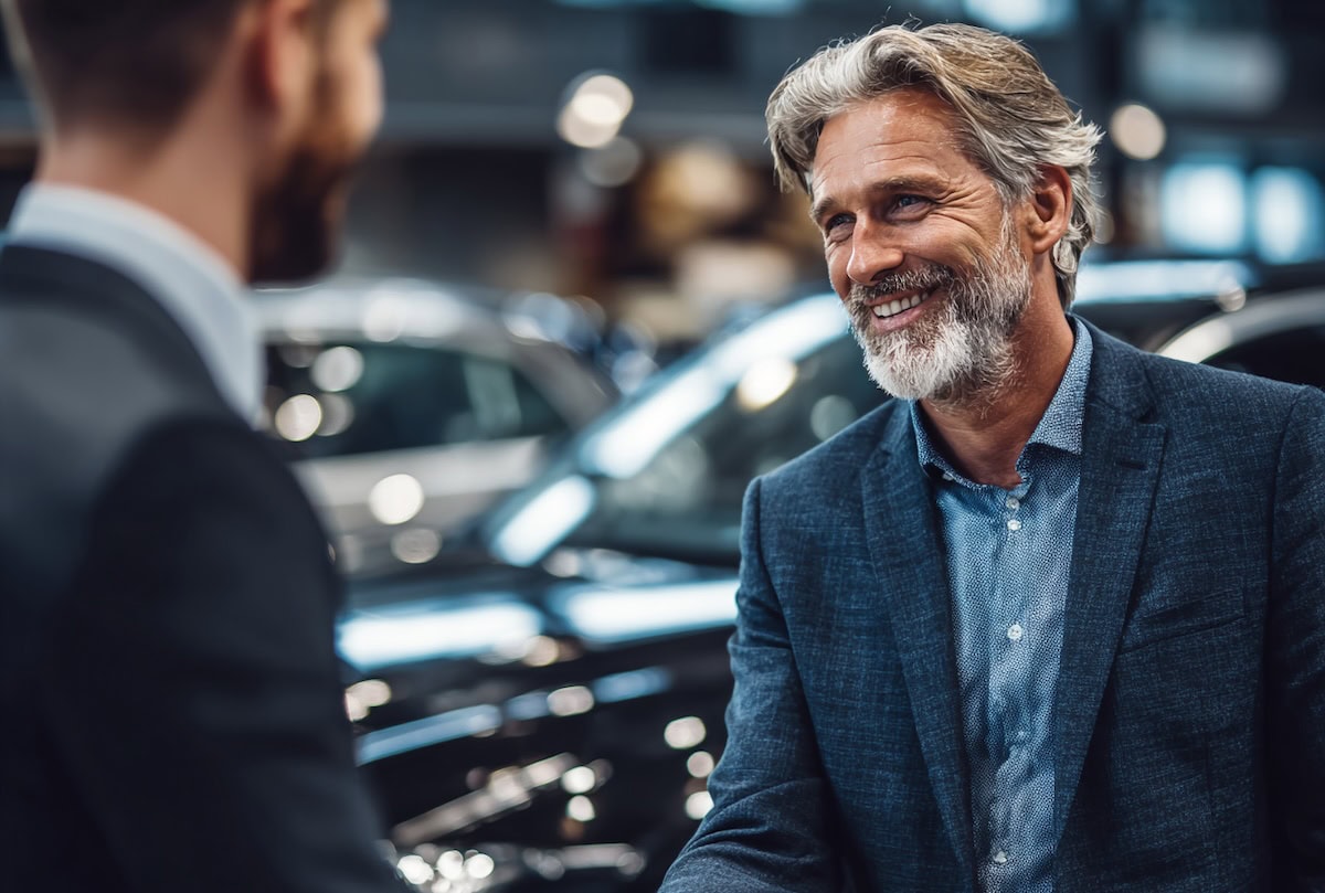Uomo che compra auto da concessionario in showroom, sorriso e conversazione amichevole, acquisto automobile di alta qualità, servizio clienti professionale, esperienza di vendita di veicoli.