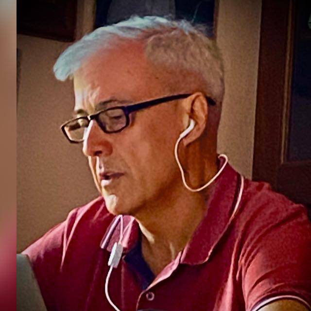 Uomo anziano con occhiali e auricolari mentre utilizza un computer, stile casual, ambiente domestico.