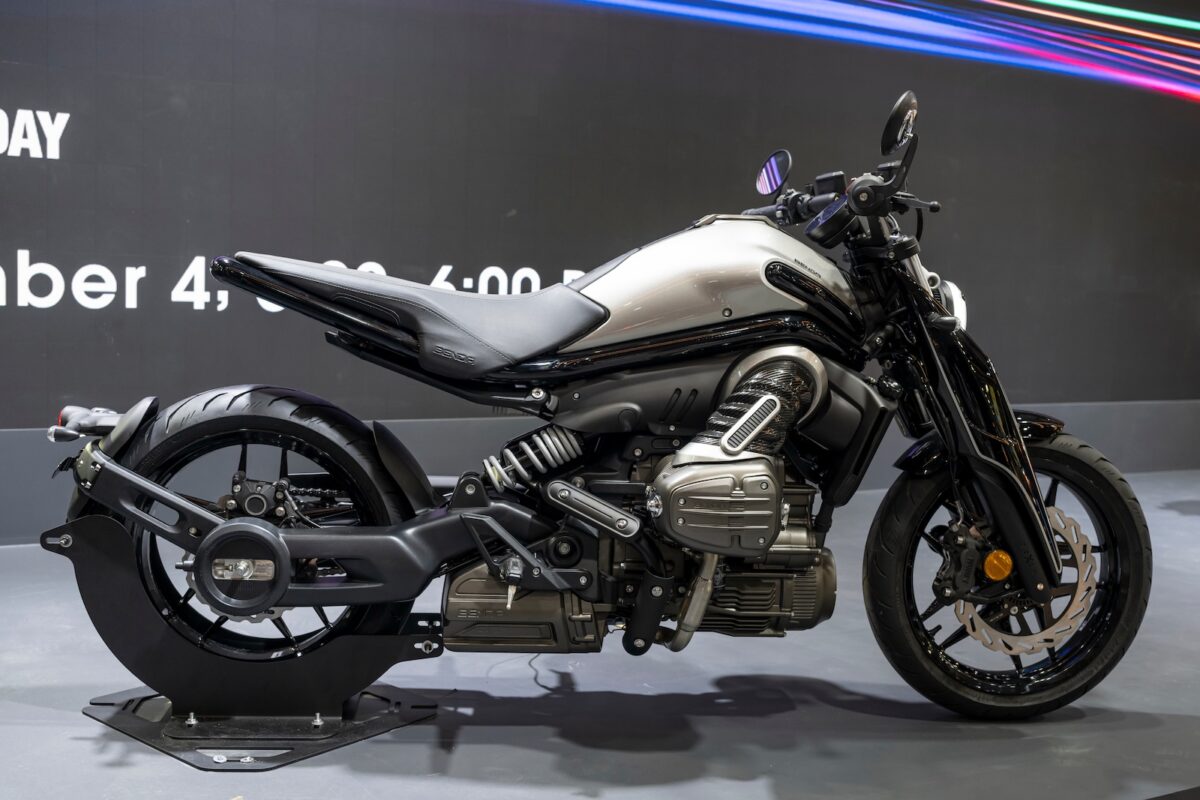 Motocicletta elettrica moderna con design audace e tecnologie innovative, esposizione in fiera con sfondo nero, ideale per appassionati di veicoli sostenibili e custom.