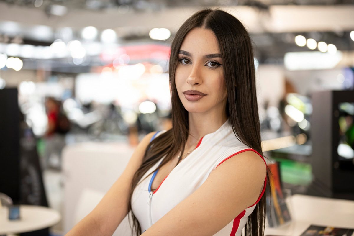 Giovane donna sorridente in un ambiente luminoso e moderno, abbigliata con abiti sportivi colorati, promozione di auto e tecnologie motoristiche.