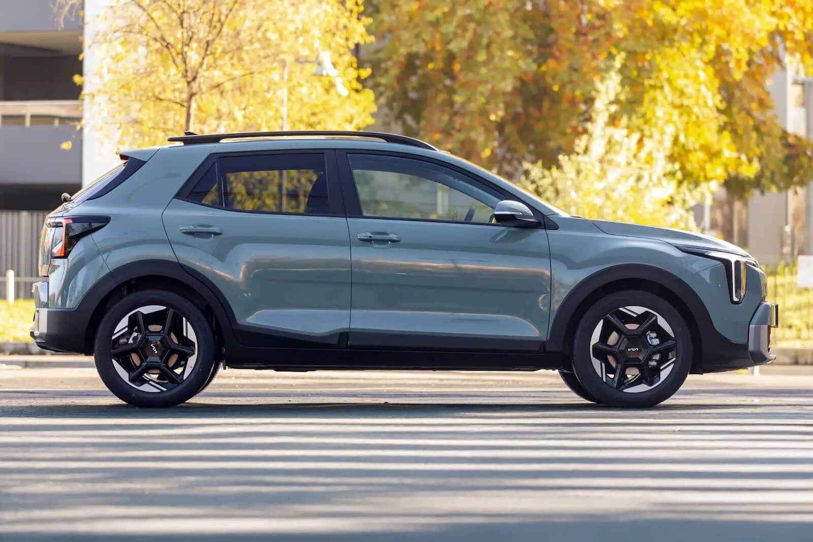 Kia Stonic 2026 grigia moderna in viaggio su strada urbana durante l'autunno con foglie cadenti e alberi colorati.