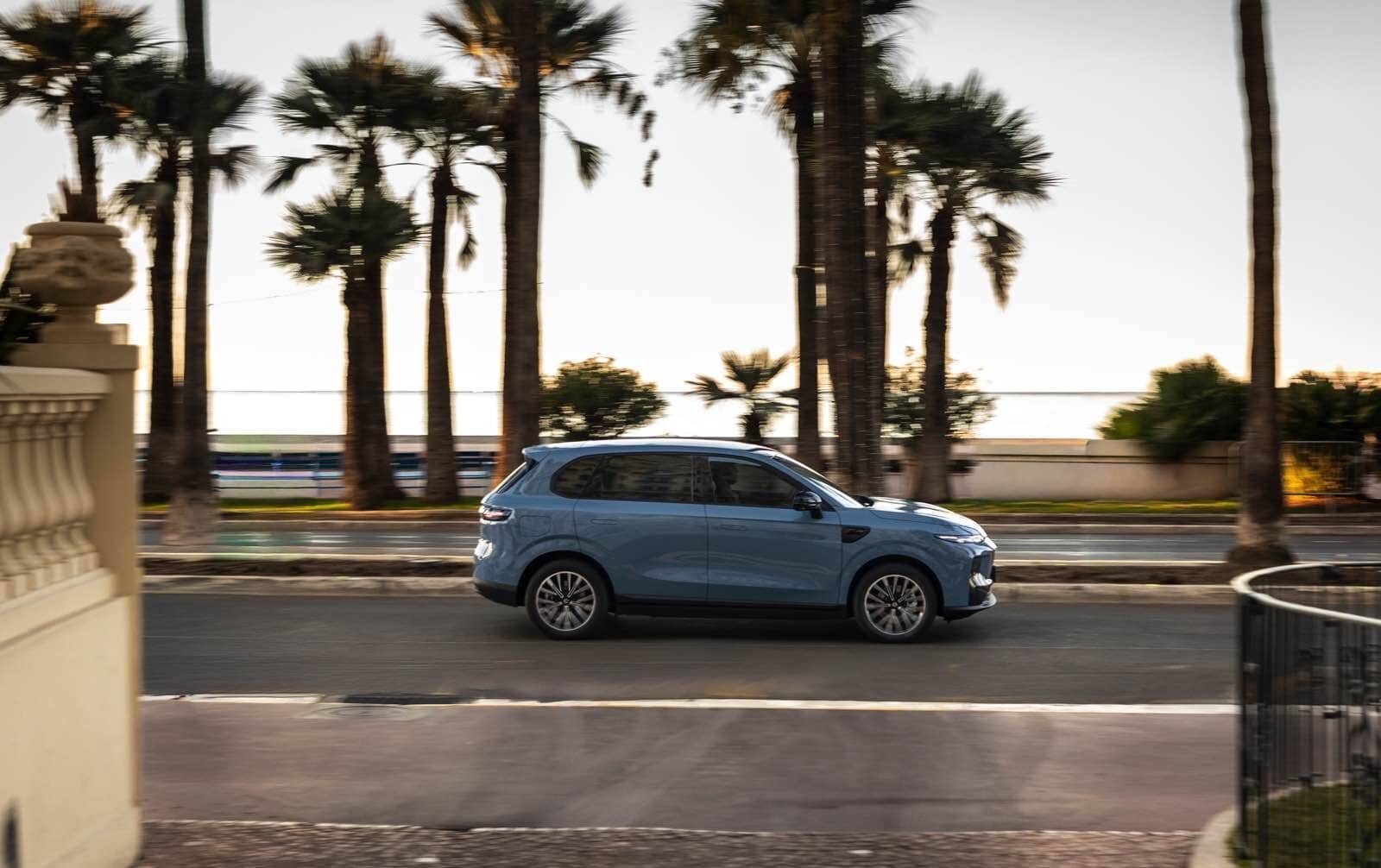 Auto SUV blu Leapmotor B10 in movimento lungo strada con palme, paesaggio soleggiato.