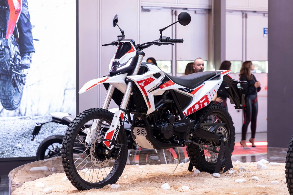 Motocicletta enduro in esposizione con pneumatici da fuoristrada, design sportivo, colori bianco e rosso, evento motori, presentazione moto da fuoristrada, veicolo off-road.