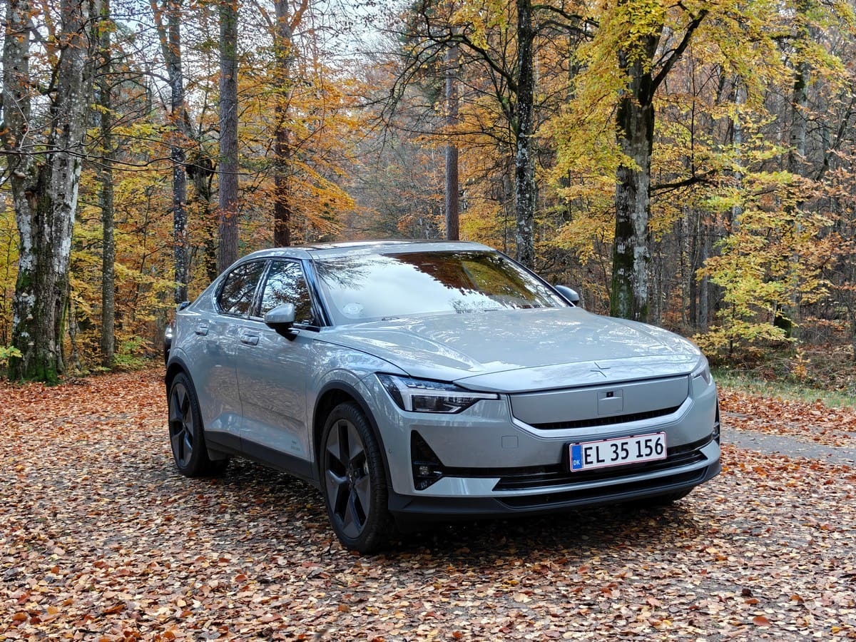 Auto elettrica moderna in un bosco autunnale con foglie cadute.