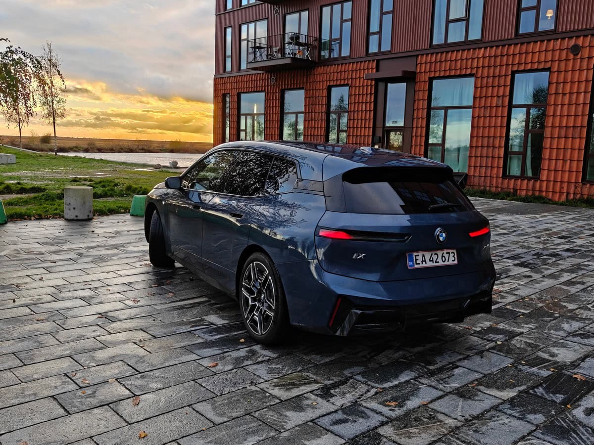 Auto elettrica BMW iX con design moderno e sostenibile, parcheggiata su una superficie pavimentata con sfondo di paesaggio naturale al tramonto, perfetta per foto auto elettriche di lusso.