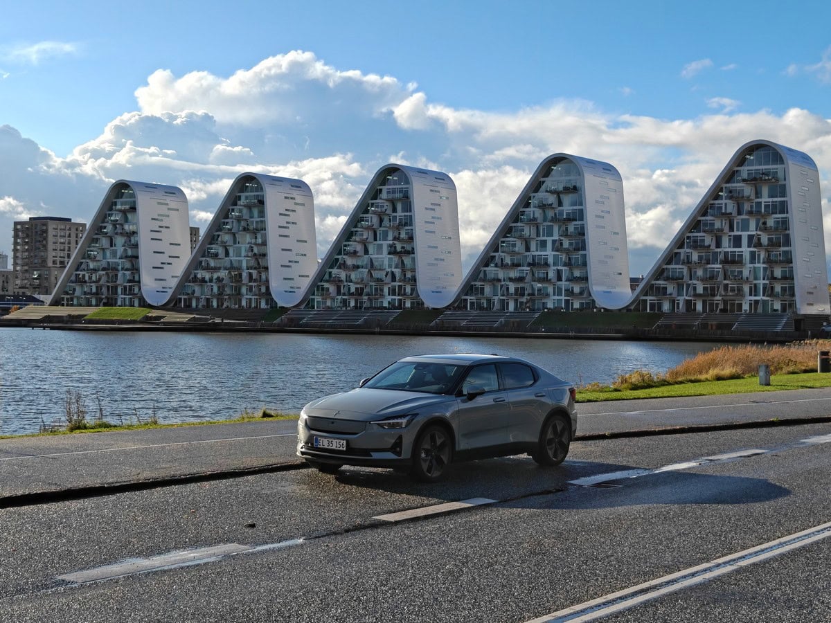 Auto elettrica grigia in primo piano con edificio innovativo sullo sfondo.