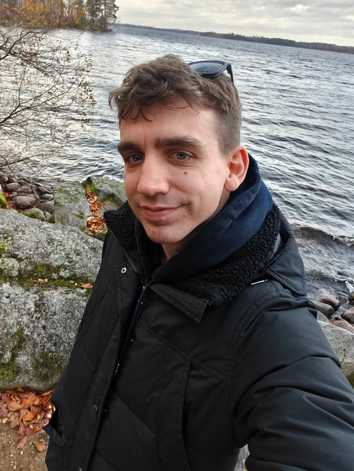 Fotografia di un giovane uomo che si gode il paesaggio lacustre in autunno, con abbigliamento da outdoor, ambiente naturale e atmosfera rilassante.