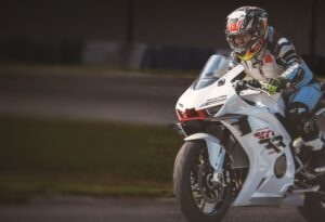 Ciclista su moto sportiva in pista, motociclista professionista con casco integrale, sportbike bianca, guida su circuito, competizione motociclistica di alta performance, motori e velocità.