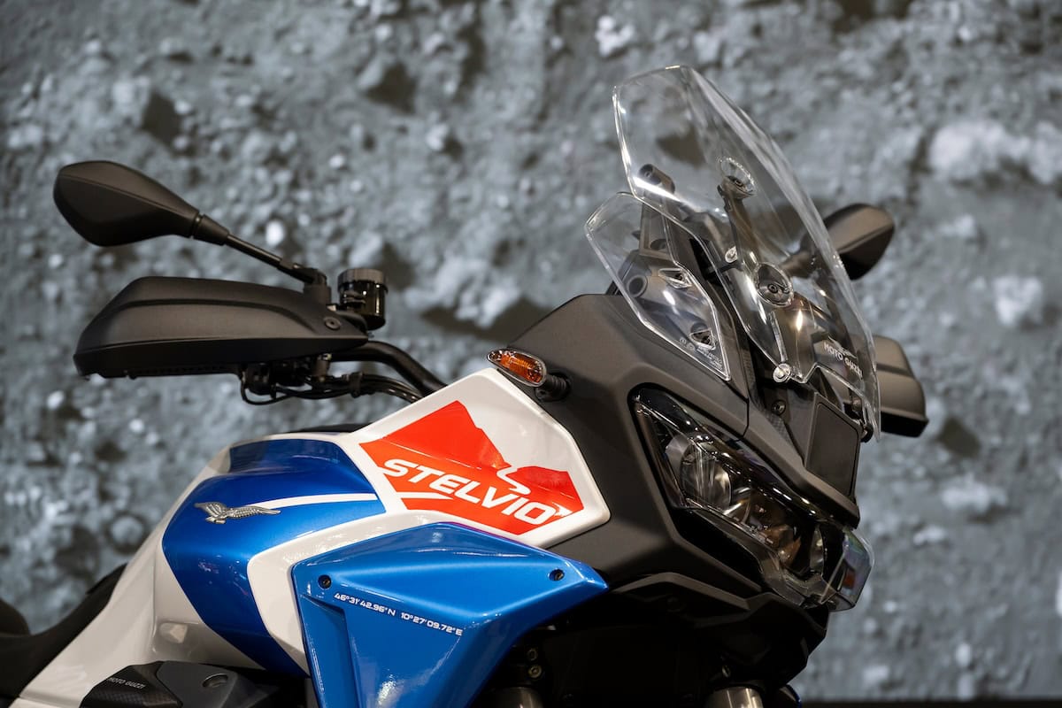 Moto Guzzi Stelvio 2026 con decalcomanie, evidenziando le linee aerodinamiche e il parabrezza trasparente su sfondo roccioso.