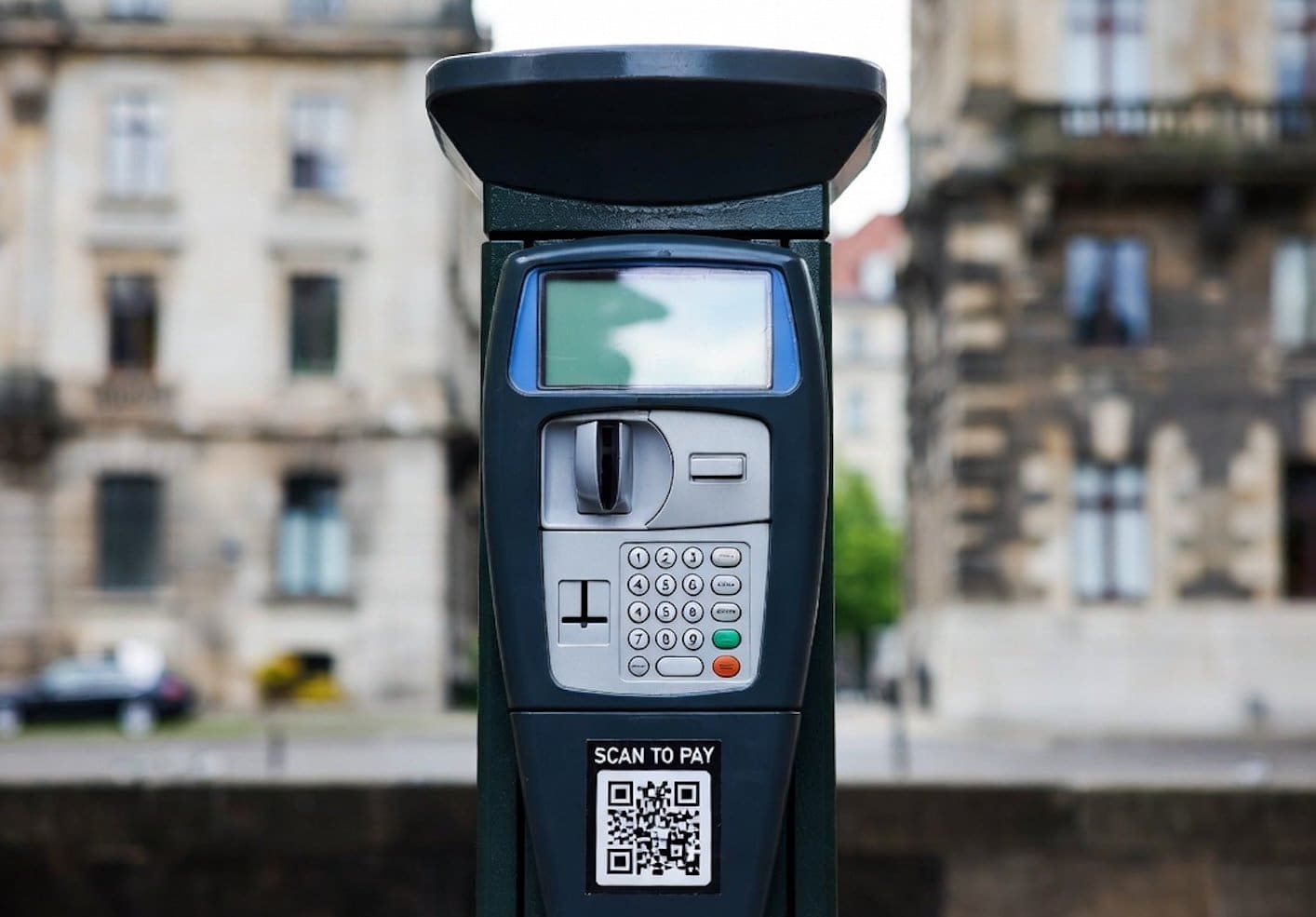 Parcometro con schermo digitale e QR code per pagamento tramite smartphone, sito per parcheggi a pagamento in città.