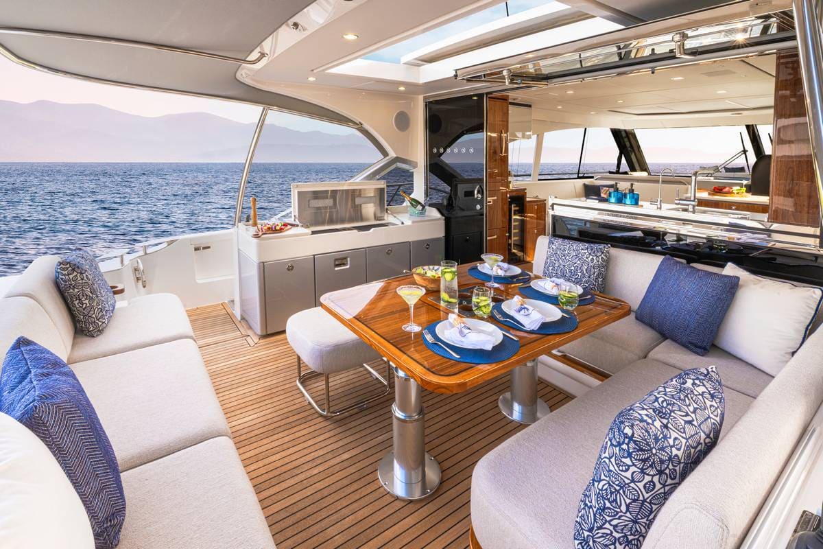 ALT: Immagine di un'ampia zona pranzo su uno yacht di lusso, con tavolo in legno e sedili imbottiti, circondata da un panorama marino mozzafiato e interni moderni.