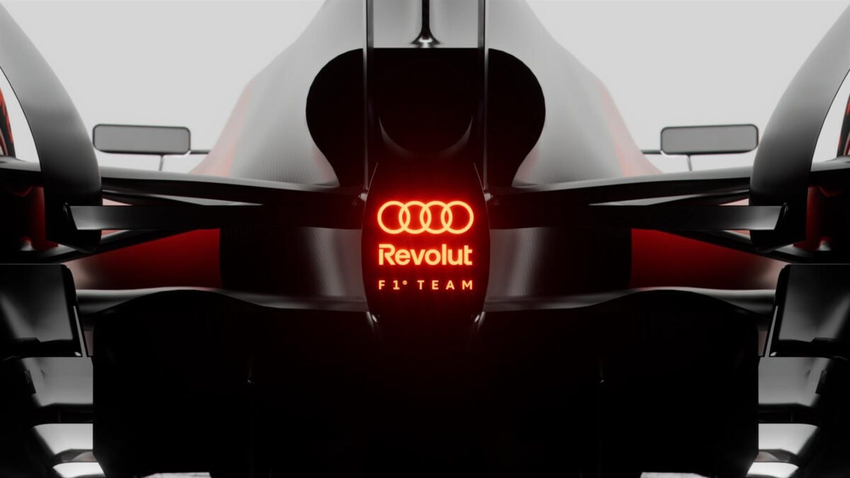Dettaglio di un'auto da corsa Formula 1 Audi Revolution con logo illuminato rosso, stile futuristico, tecnologia avanzata, progettata per alte performance in circuito.