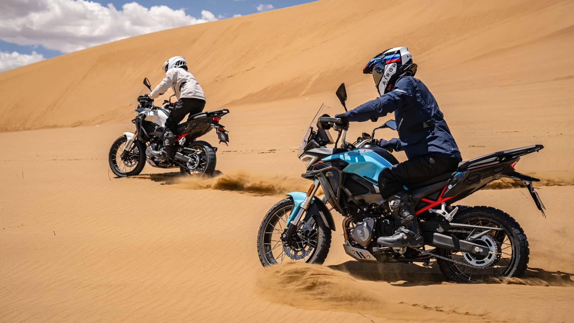Motociclisti su moto Morbidelli T352X in ambientazione desertica con dune e cielo nuvoloso.