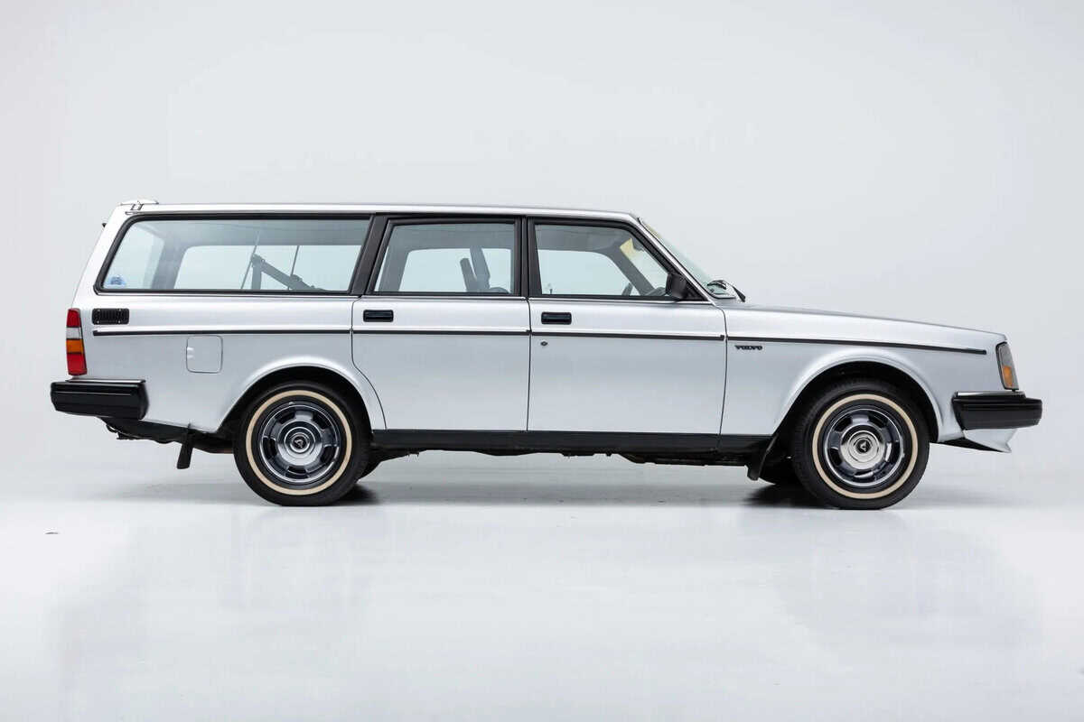 Volvo 245 Station Wagon argento, profilo laterale sinistro, sfondo bianco minimalista.