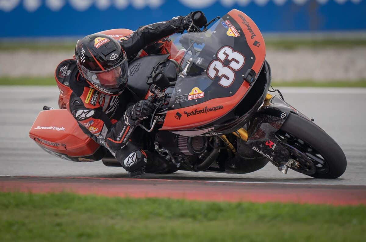 Motocicletta Harley-Davidson in curva su pista, vista laterale. Pilotata, sponsor visibili sulla carena rossa.