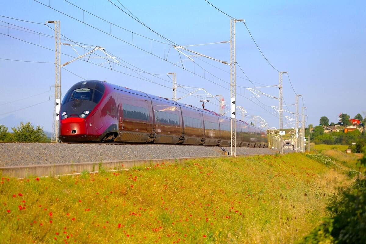 Italo AGV 575 treno rosso su binario di campagna, vista laterale, estate.