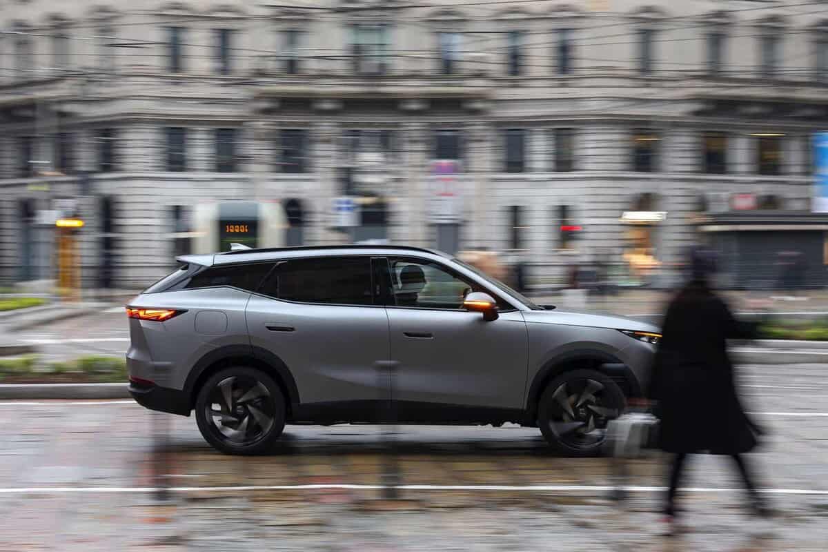 Omoda 7 SHS-P grigia, vista laterale. Strada urbana, persona in movimento. Ambiente cittadino.