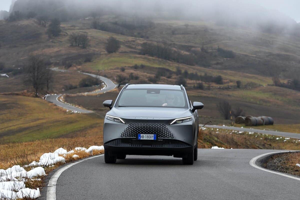  Omoda 7 SHS-P grigia su strada di montagna, vista frontale, paesaggio collinare innevato, guidatore visibile.