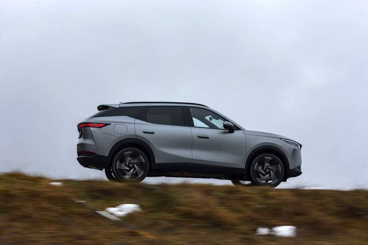 SUV Omoda 7 SHS-P grigio silver, angolazione laterale, in movimento su strada collinare.