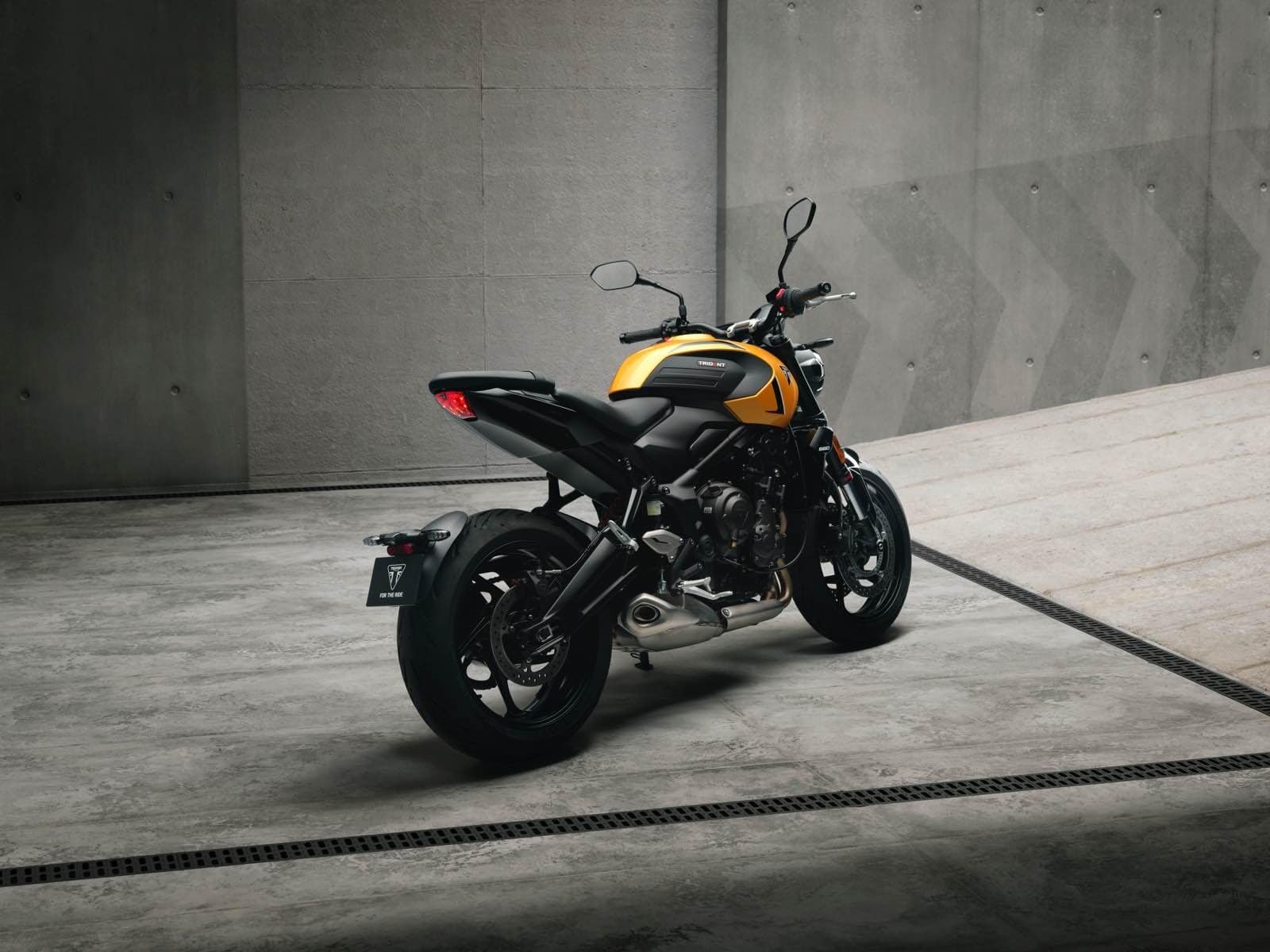 Motocicletta Triumph Trident 660 naked nera e gialla posizionata su un pavimento di cemento, con pareti di cemento sullo sfondo.