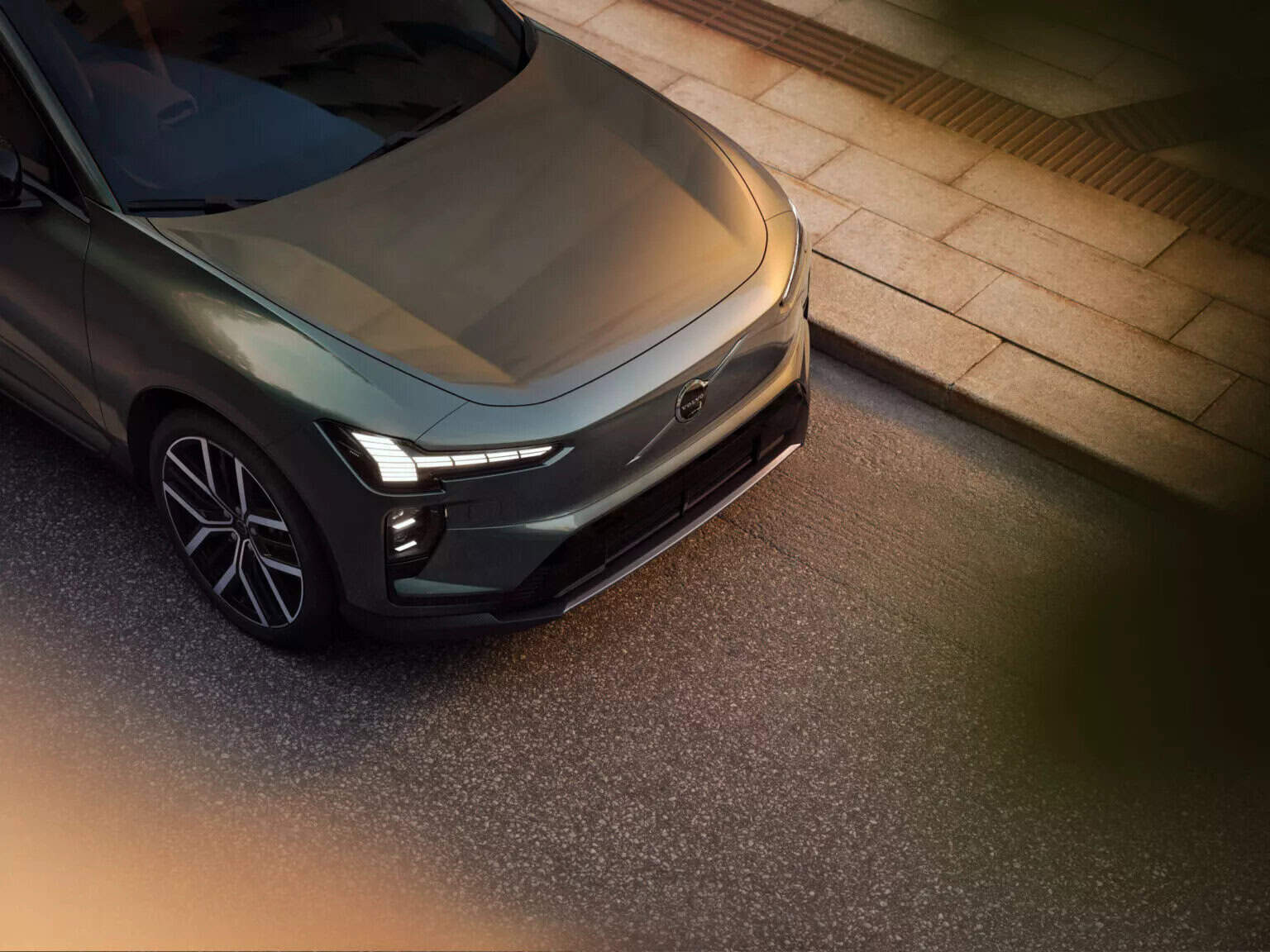 Volvo EX60 grigio vista dall'alto, strada urbana, design sportivo, luci LED moderne.