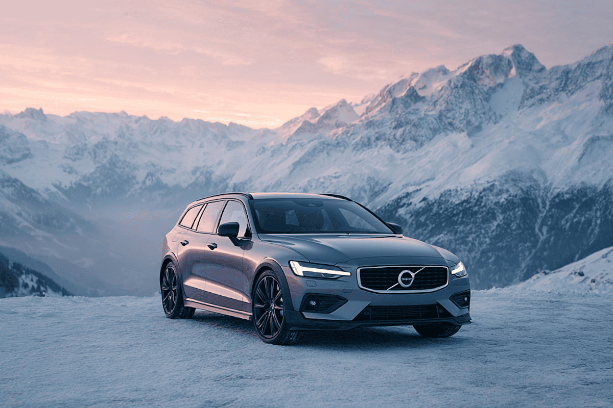 Volvo V60 grigia su neve, montagne innevate sullo sfondo, vista frontale laterale, al tramonto.