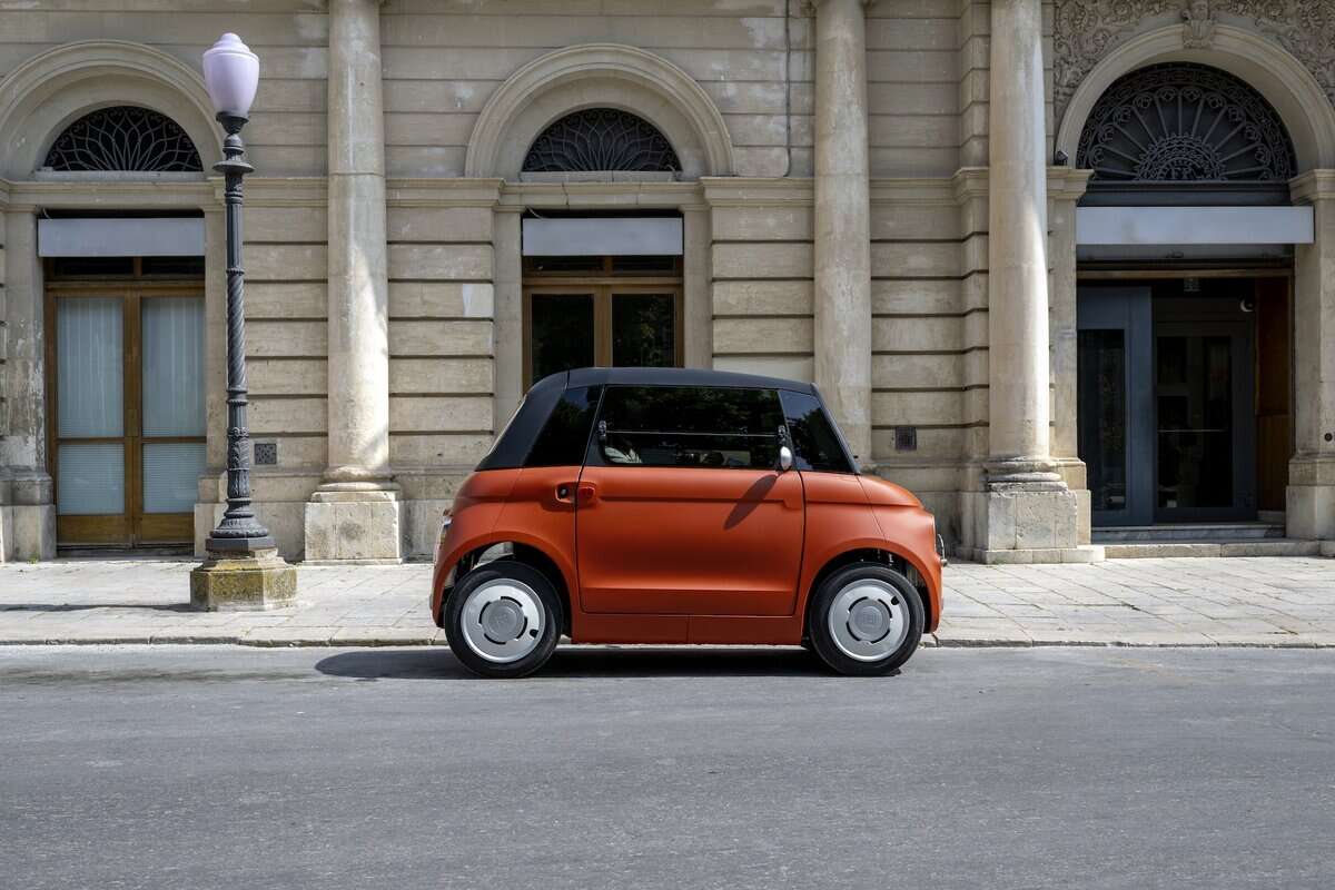 Fiat Topolino Corallo in strada cittadina, vista di profilo su edificio storico in pietra.