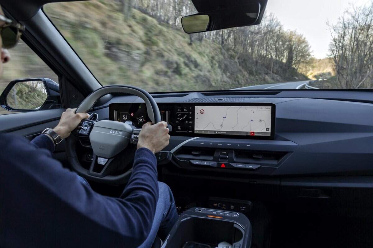Guidatore in auto elettrica Kia EV5, navigatore acceso, strada panoramica boschiva.