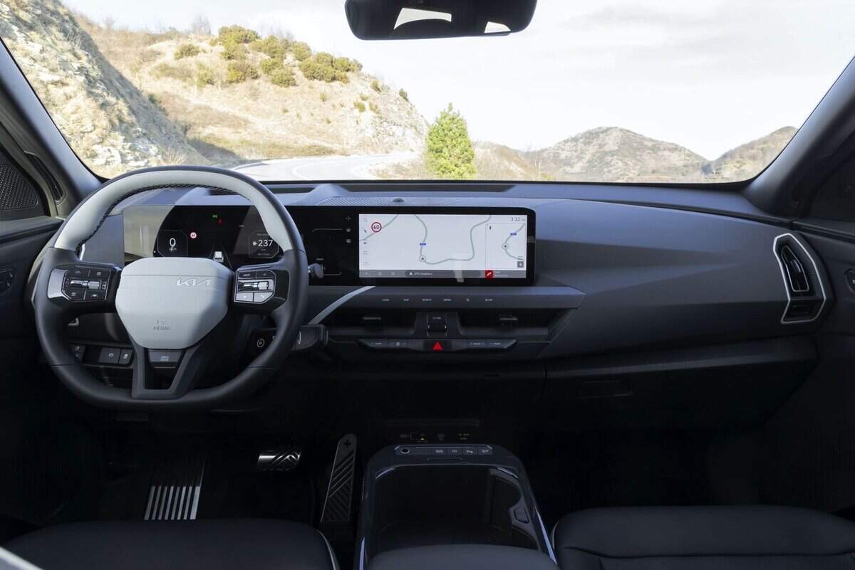Interni auto Kia EV5, volante e display touchscreen, vista strada montagna.