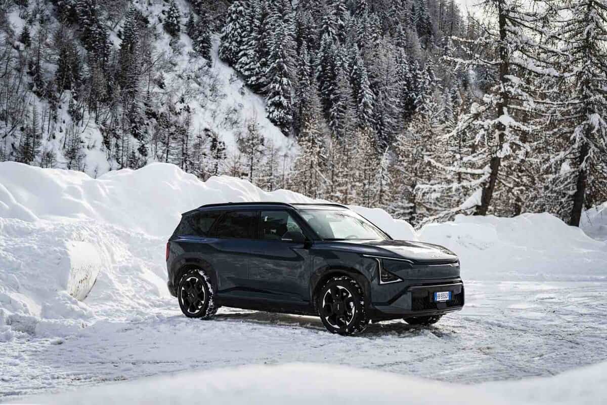 SUV Kia EV5 nero sulla neve, ambiente montano, inverno, vista laterale sinistra, foresta innevata sullo sfondo.