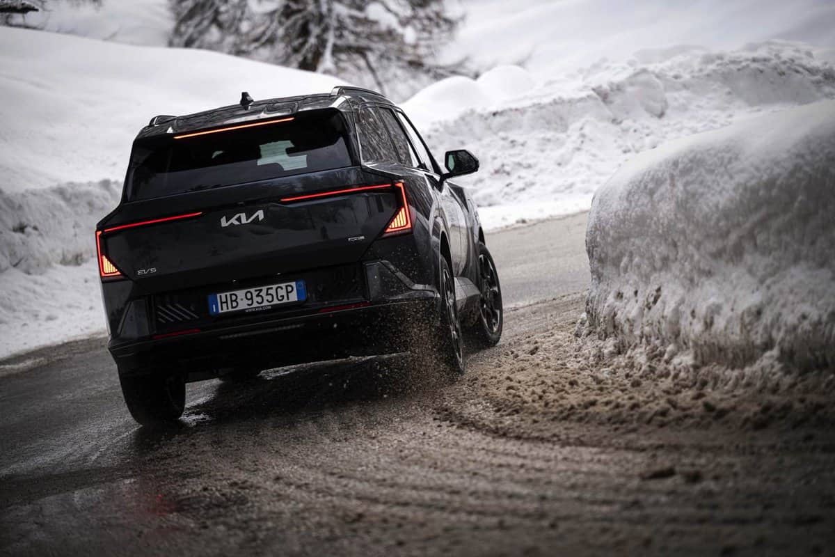 Kia EV5 in curva su strada innevata, vista posteriore, guida sicura su ghiaccio.