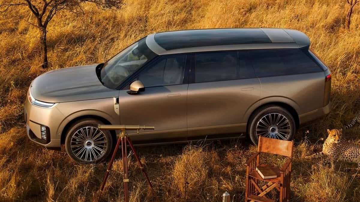 SUV XPeng GX visto di lato in savana, vicino telescopio e ghepardo, sedie in legno sullo sfondo.