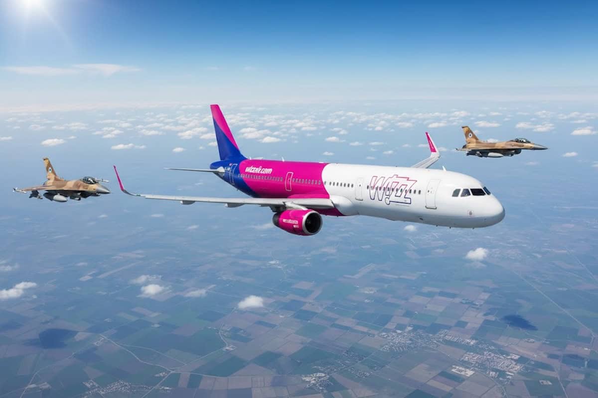 Wizz Air Airbus A321 in volo accanto a due jet militari F-16 sopra un paesaggio rurale, vista aerea.