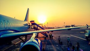 Aereo in partenza all'aeroporto al tramonto con passeggeri che caricano bagagli sullo sfondo.