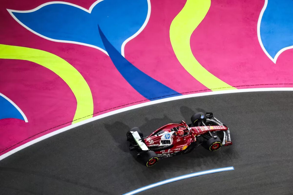 Charles Leclerc al volante della Ferrari F1 2025 durante una curva su asfalto nero, con fondo colorato rosa, giallo e blu che contrasta vivacemente con la monoposto rossa in azione.