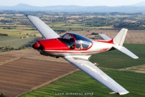Aereo di piccole dimensioni rosso e bianco in volo su un campo.