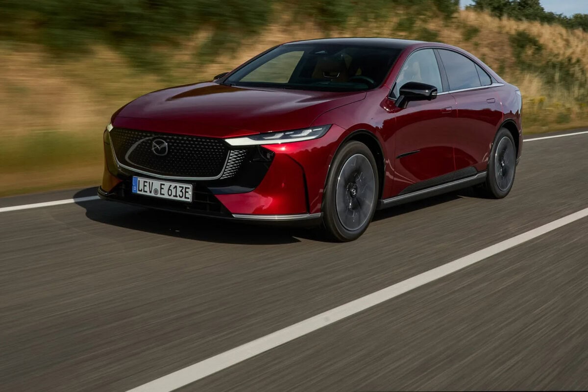 Mazda 6e 2025 rossa in movimento su strada con fondo scuro e vegetazione sullo sfondo.