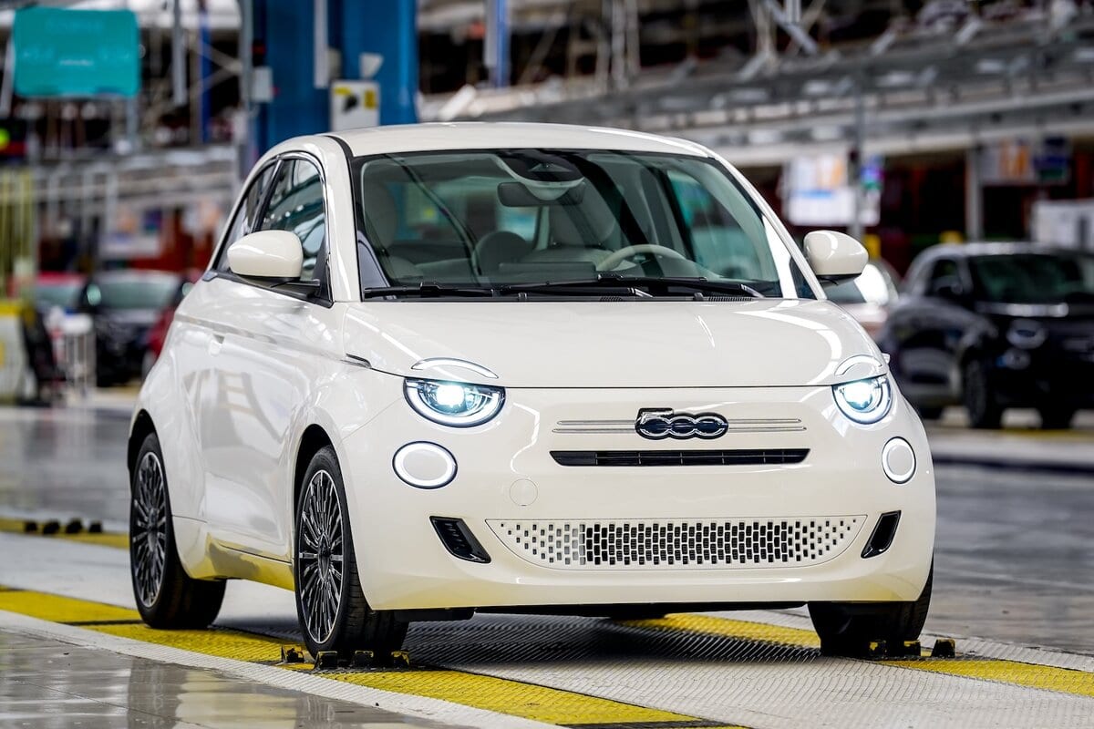 Vista frontale della Fiat 500 ibrida bianca in fabbrica con fari LED accesi e design compatto elegante