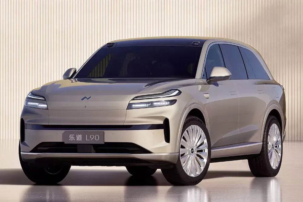 Onvo L90 SUV elettrico beige in vista frontale tre quarti, posizionato in uno studio con sfondo neutro e illuminazione uniforme.