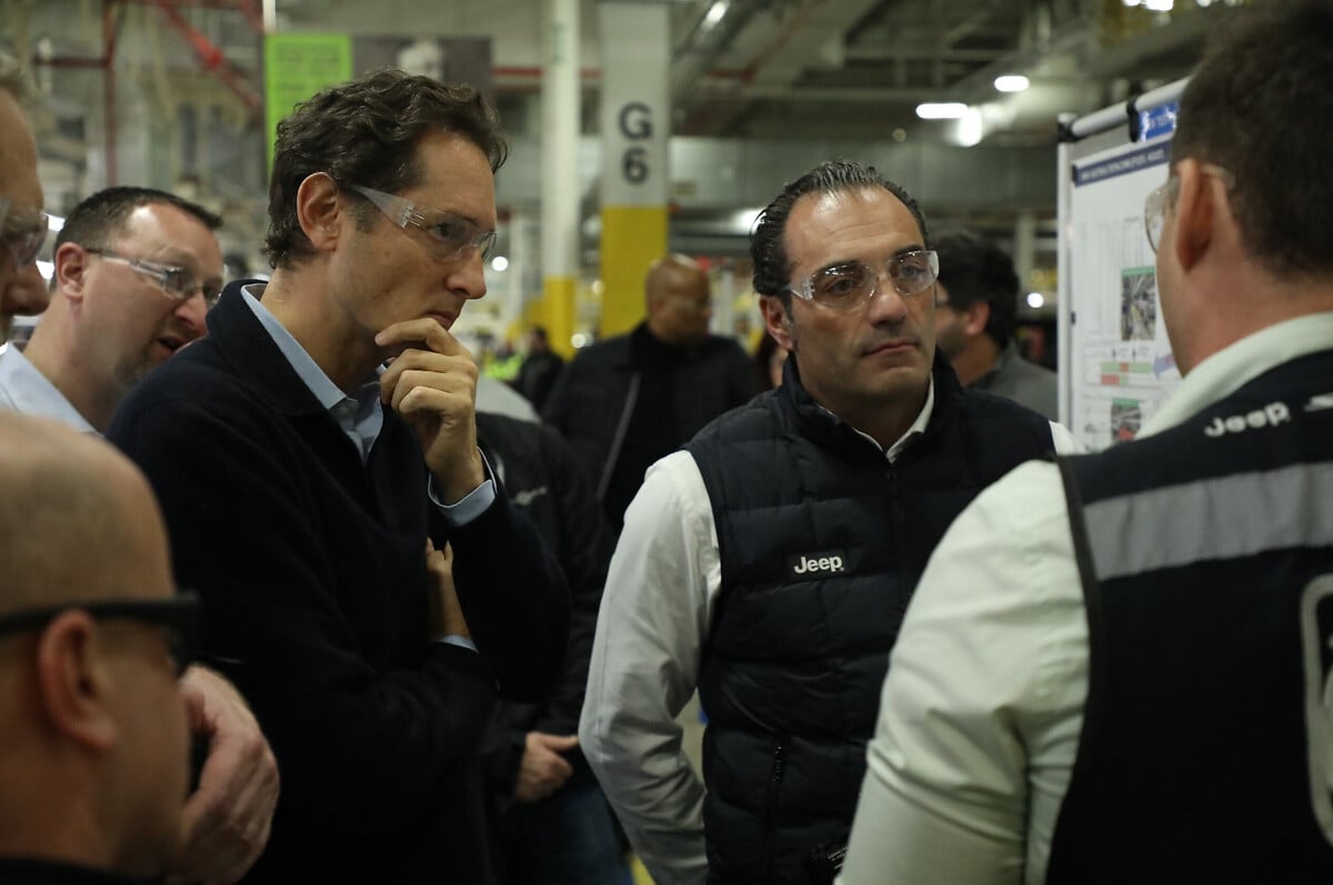 Antonio Filosa e John Elkann osservano attentamente una presentazione tecnica durante una visita in fabbrica Jeep. Entrambi indossano occhiali protettivi e abbigliamento da lavoro mentre ascoltano un membro del team.