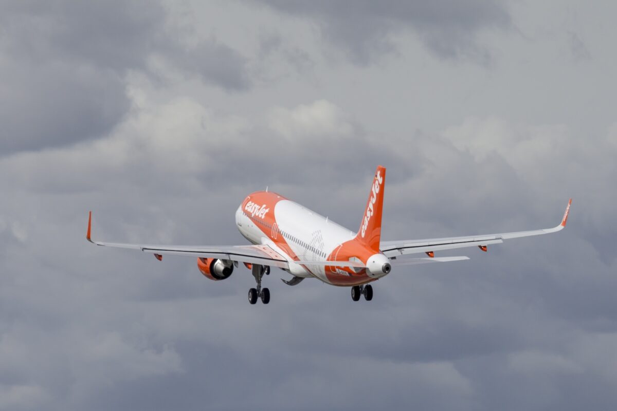 Airbus A320 easyJet arancione e bianco in fase di decollo, ripreso da dietro mentre si alza tra le nuvole grigie.