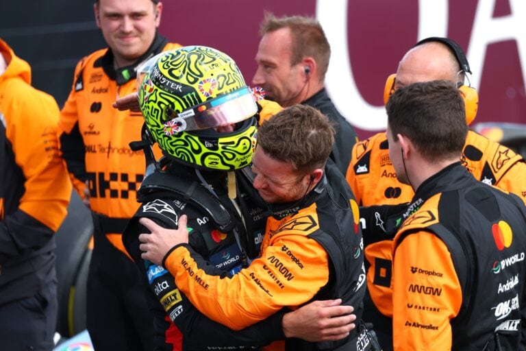 Lando Norris abbraccia un membro del team McLaren dopo la vittoria nel GP di Silverstone 2025, circondato dai meccanici in tuta arancione.