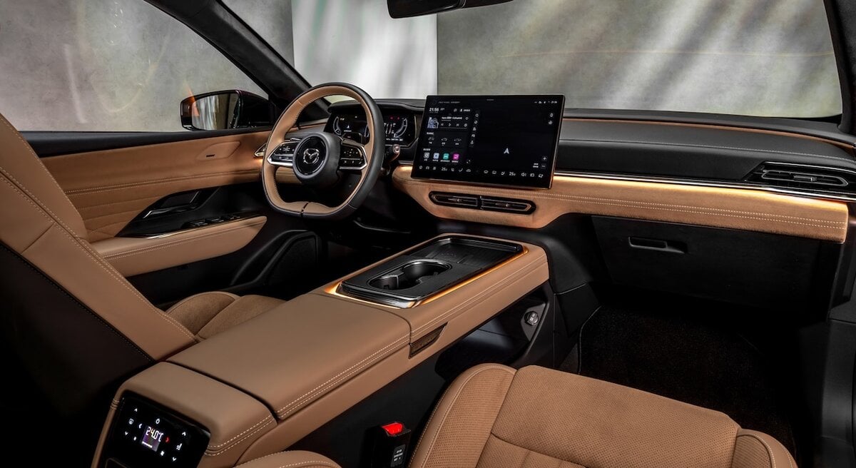 Interni della Mazda 6e 2025 con plancia digitale, schermo touchscreen e sedili in pelle marrone.