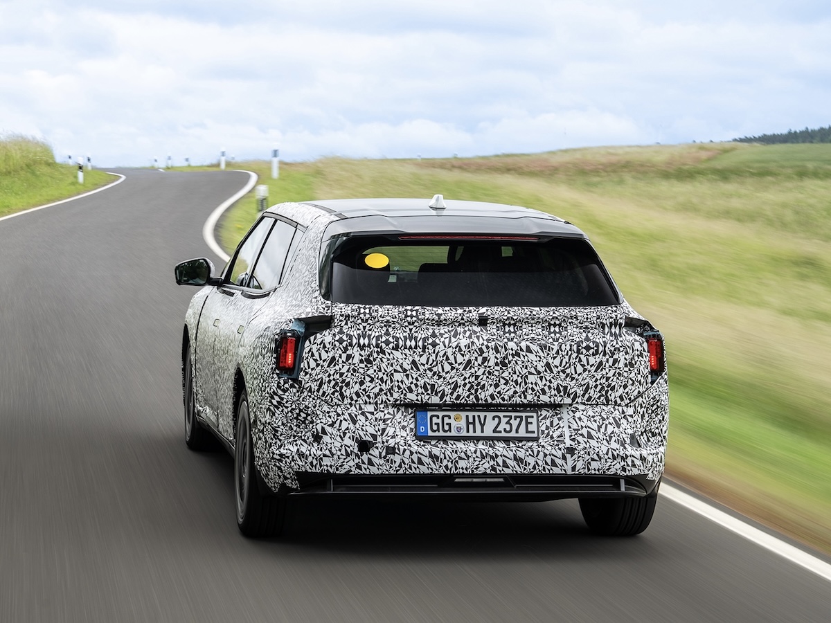 Vista posteriore del prototipo Kia EV4 camuffato su una strada di campagna, con targa di prova tedesca. Il veicolo mostra proporzioni da crossover elettrico con un look aerodinamico.