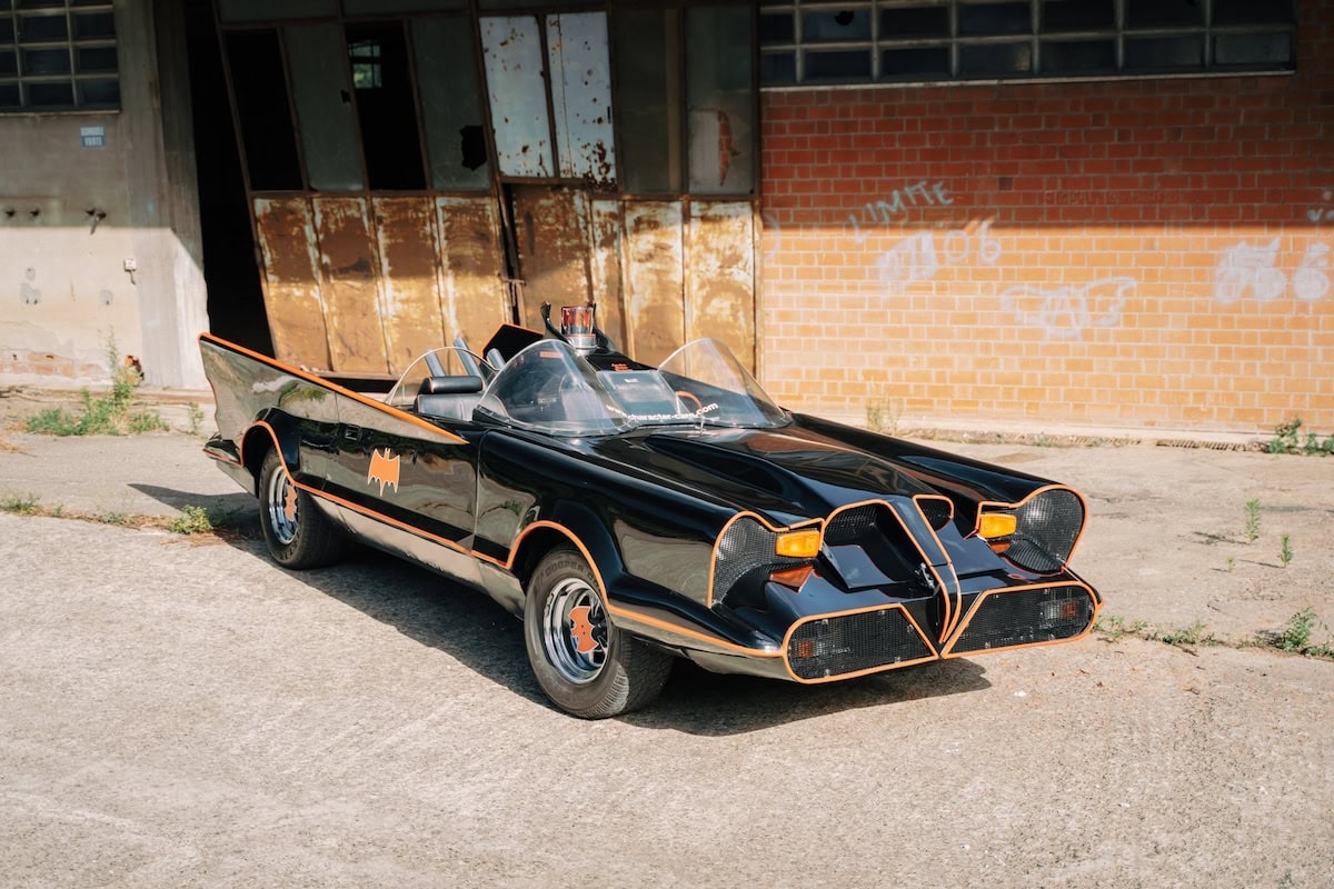 Replica della Batmobile classica nera con bordi arancioni parcheggiata davanti a un edificio industriale.